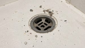 A corroded metal shower drain cover being removed for inspection.